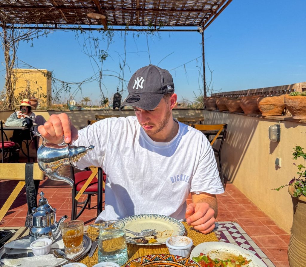 Rooftop terrace in Marrakech. a man is drinking some mint tea. The table is filled with amazing Moroccan food