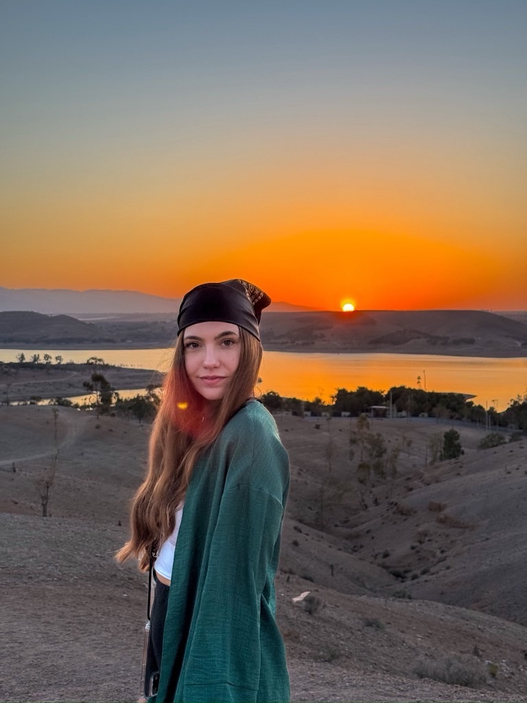 A women standing in the Agafay Desert in Morocco. Behind her the sun sets. 